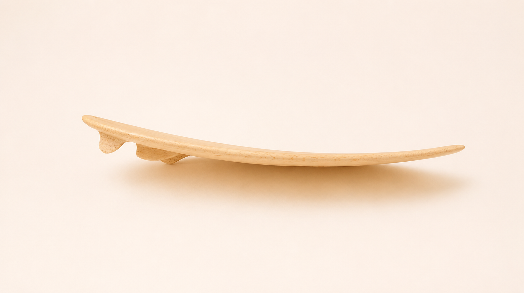 A light natural wooden finger surfboard with three fins, viewed from the side, displaying the board's curvature - ideal for catching the breeze.