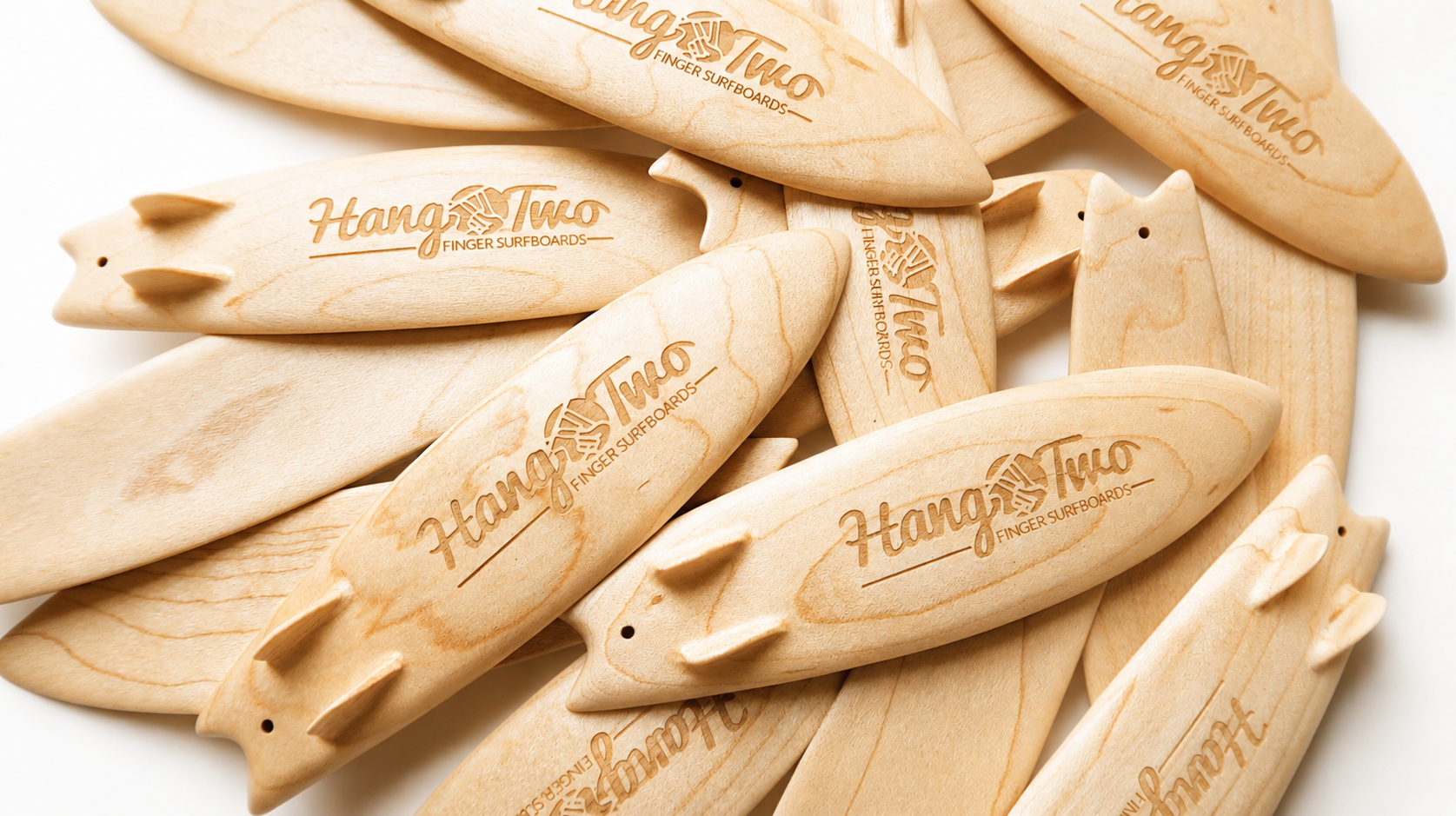 A pile of small natural wood surfboards engraved with 'Hang Two Finger Surfboards' on a white background.