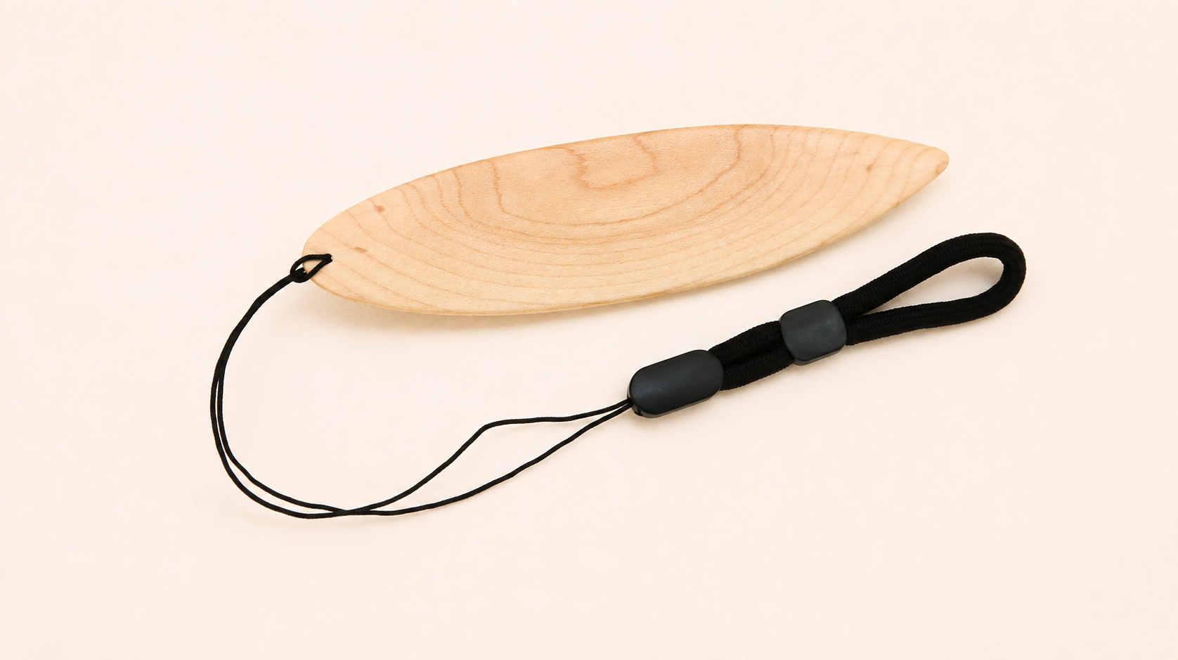 A light natural wood surfboard-shaped toy for flying out the car window, with a black cord loop and black plastic connector, photographed on a plain off-white background.