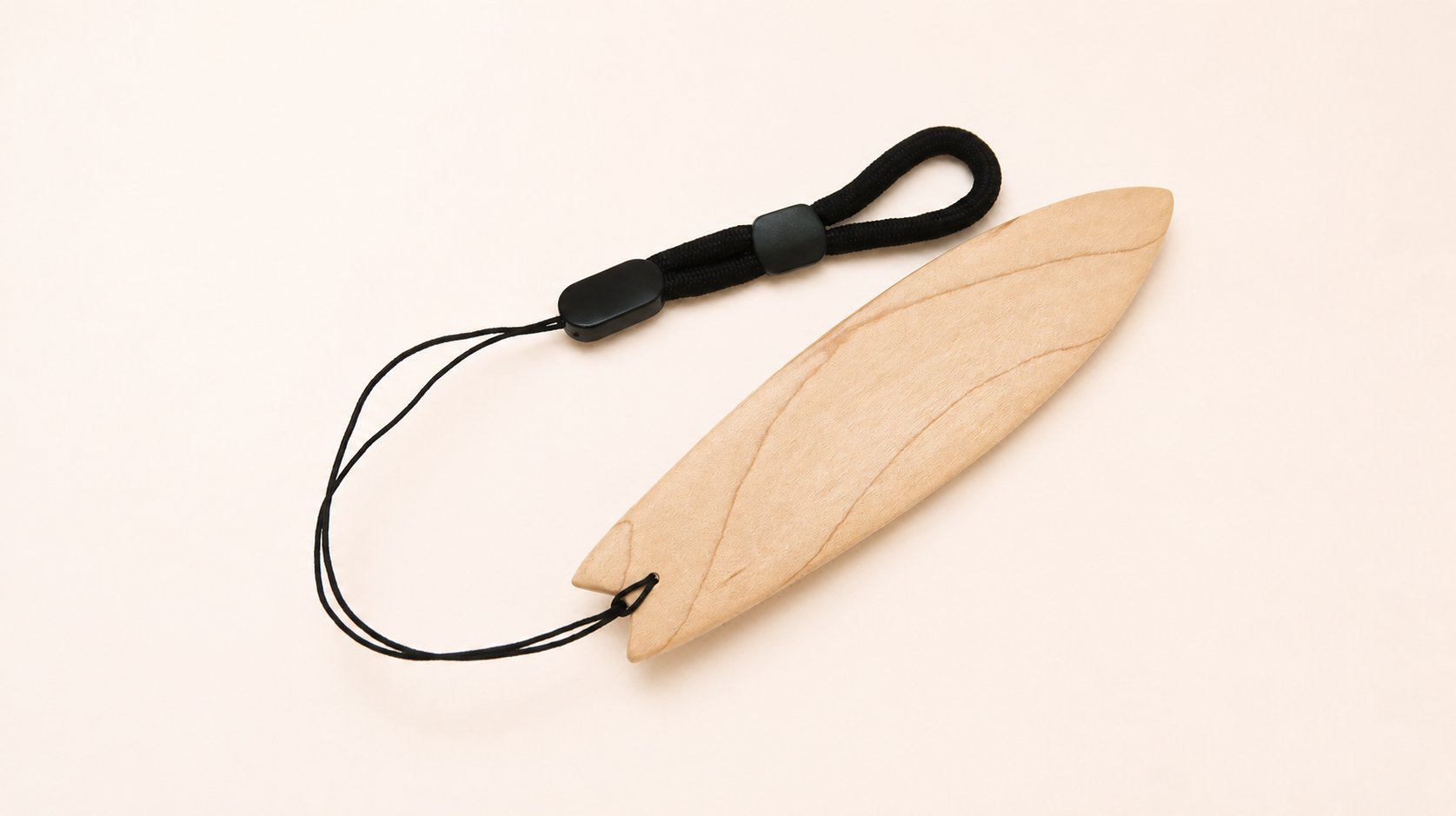 A light natural wood surfboard accessory with a black cord loop and black plastic clasp, photographed on a plain warm off-white background.