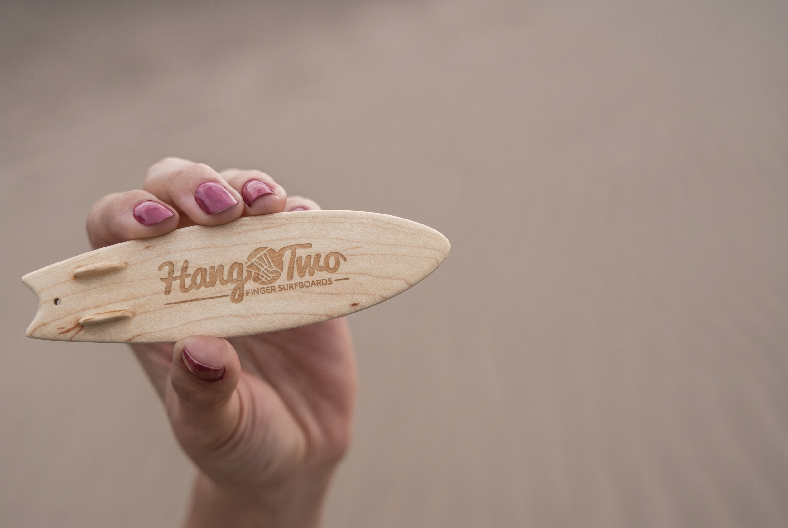 A person's hand holding a 5 inch wooden surfboard engraved with the logo Hang Two Finger Surfboards.